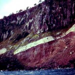 Seacliff near Green Island showing the basaltic andesite lava flow with a yellow sulphur-rich layer immediately beneath it and orange hydrothermally altered rocks in lower seacliff.